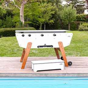 Table de baby-foot d’extérieur blanche Stella Star sur terrasse avec banc et roulettes.